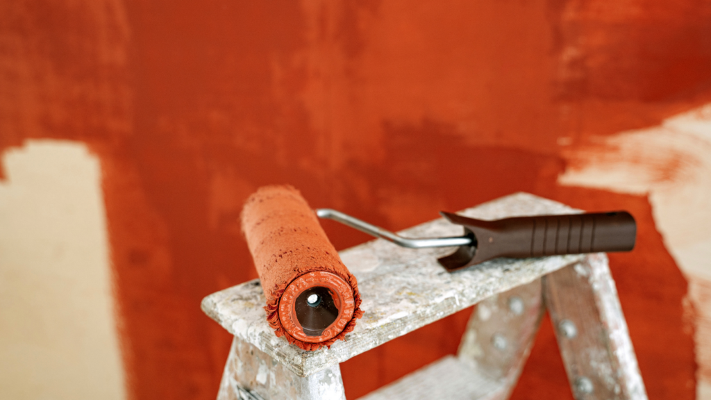 a red paint roller sitting on a step ladder in front of a red painted wall.