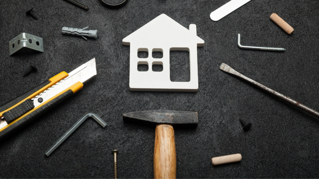 various small hand tools and accessories laid out on a black backdrop, centered around a cutout of a house.