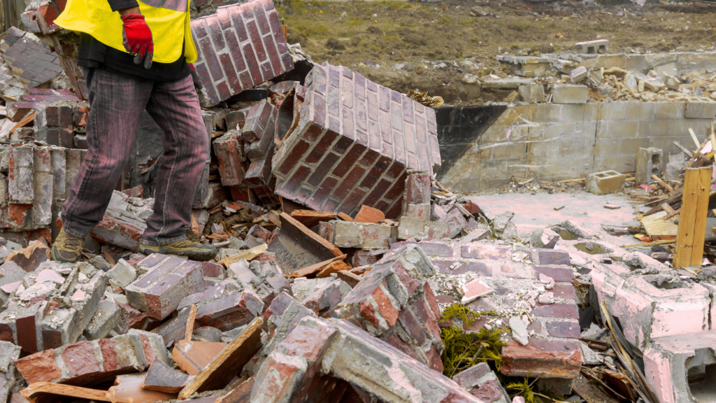 a person in a yellow safety vest walking through a pile of demolished rubble.