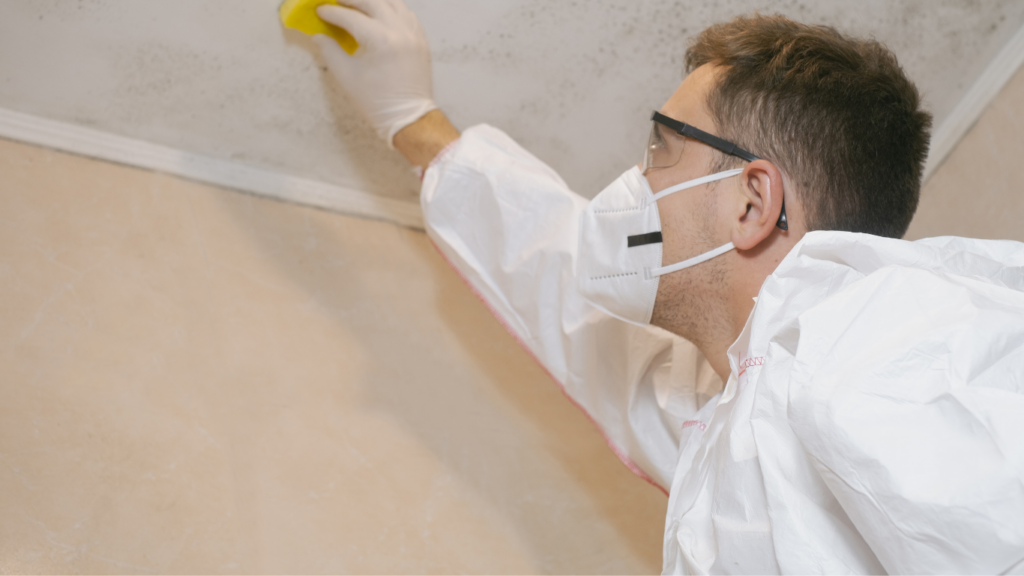 a man in protective gear using a sponge on the ceiling to test mold.