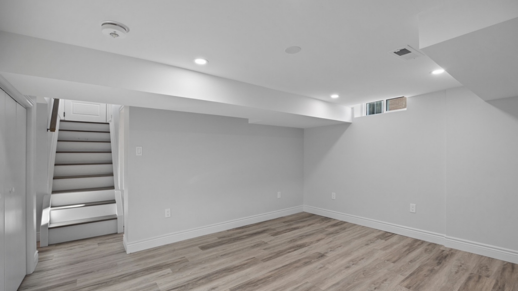 An empty basement with white walls and hardwood floors