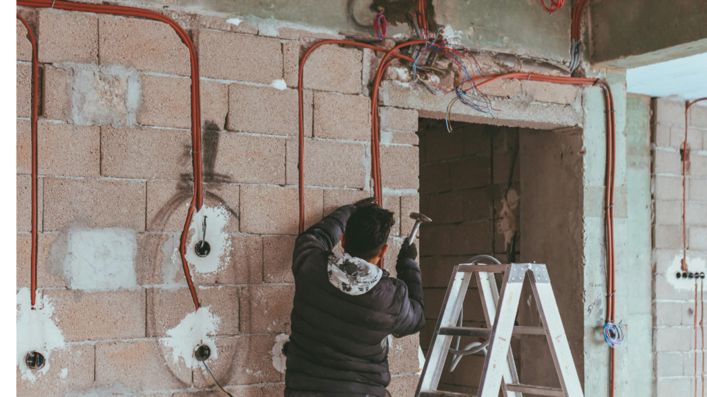 a man next to a ladder working with a hammer on a cement brick wall.